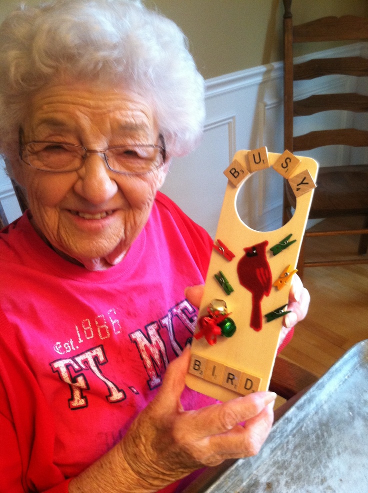 an older woman holding up a wooden letter shaped object with birds on it's sides