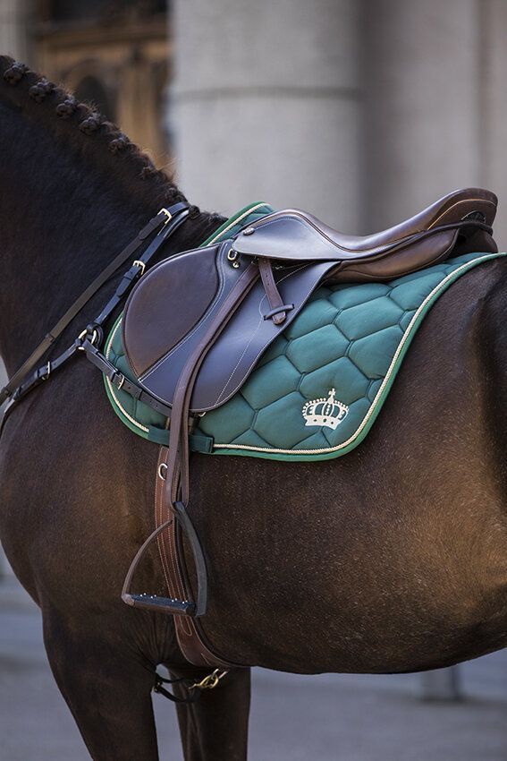 a brown horse with a green saddle on it's back standing in front of a building