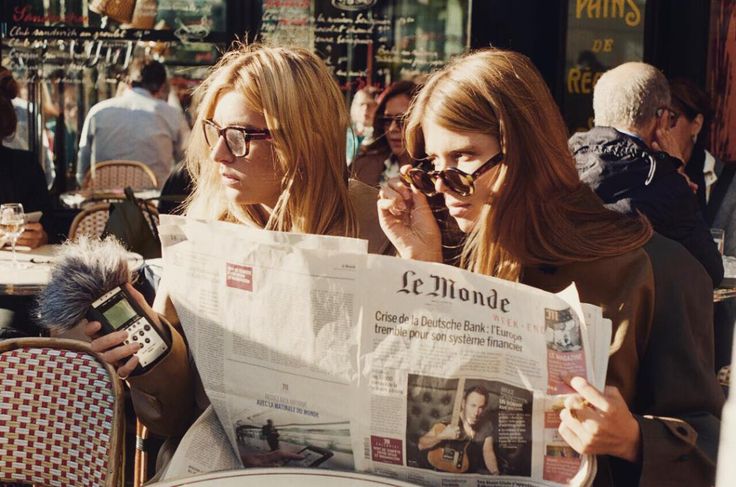 two young women sitting at an outdoor table reading a newspaper