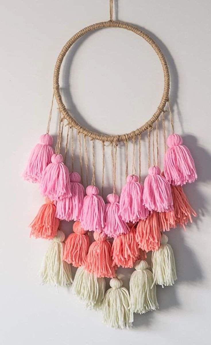 a pink and white wall hanging with tassels in the shape of a circle