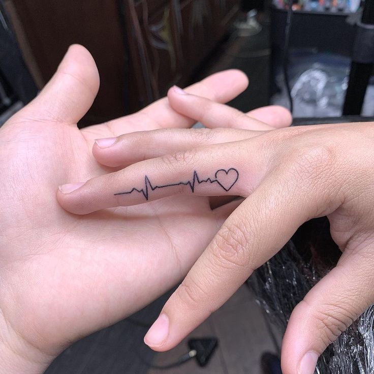 two hands holding each other with a heartbeat tattoo on their thumb and ring finger,