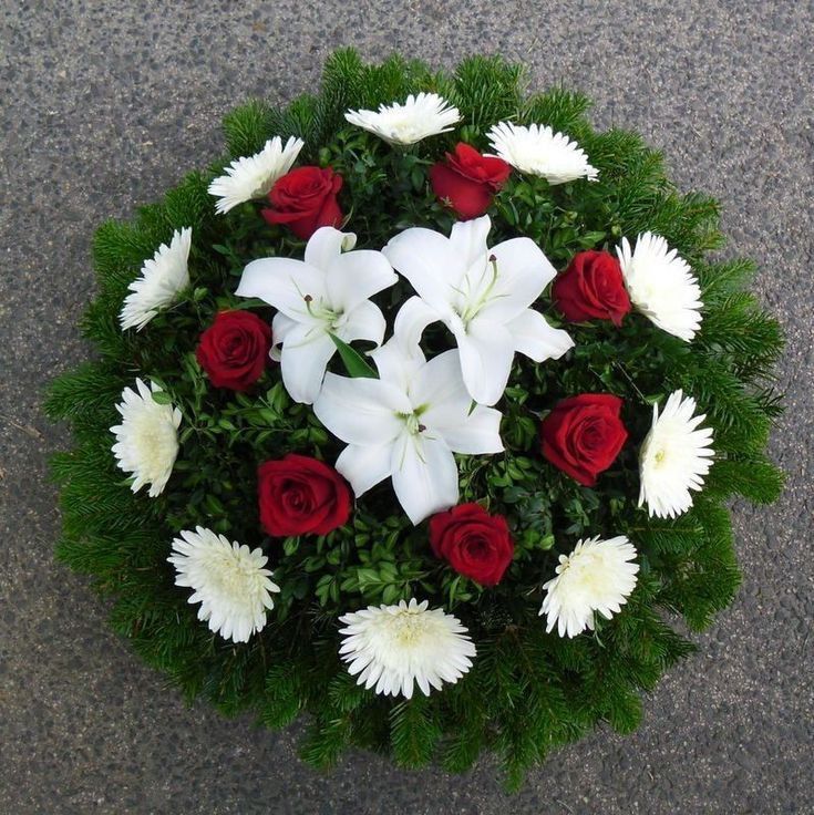 white and red flowers arranged in a circular arrangement on the ground with greenery around them