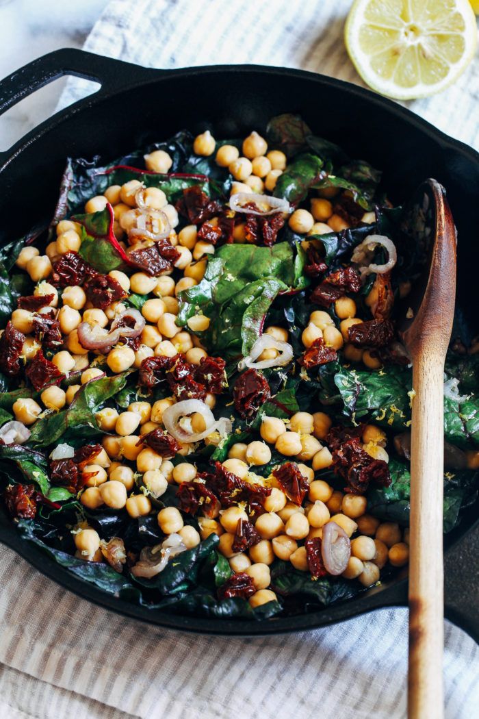 a skillet filled with chickpeas, spinach and other vegetables next to a wooden spoon