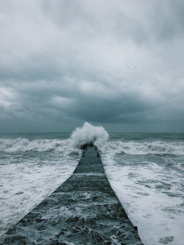 a long pier extending into the ocean with waves crashing on it and people standing at the end