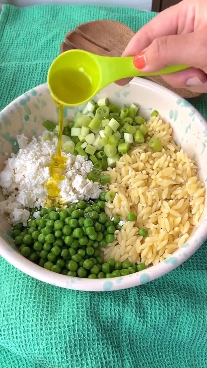 someone pouring dressing into a bowl filled with rice, peas, and other foodstuffs