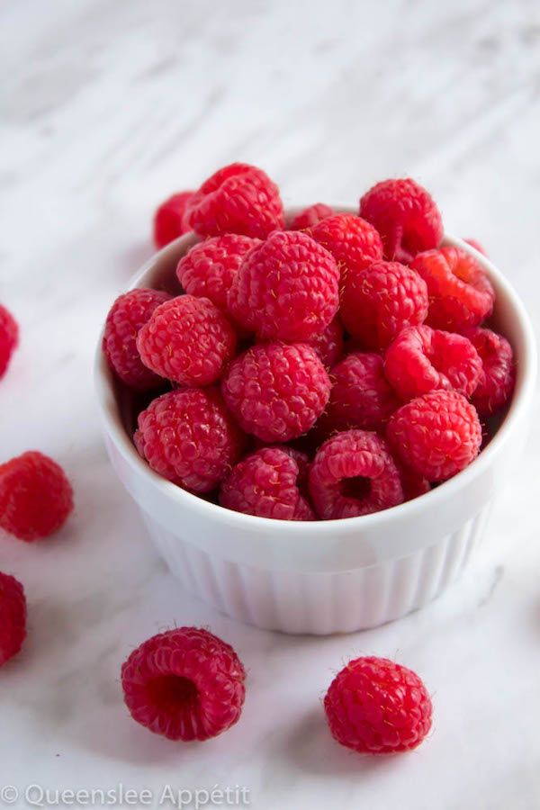 raspberries in a white bowl on a marble surface