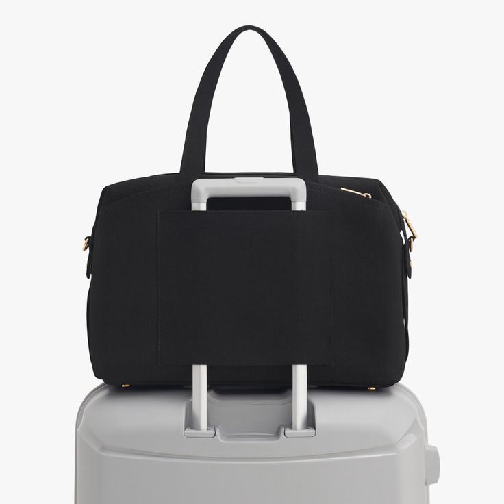 a black handbag sitting on top of a white suitcase with handles and zippers