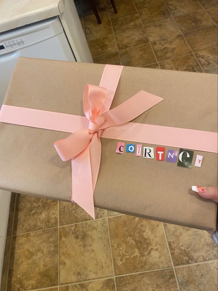 a person holding a wrapped gift with the word gourmet on it and pink ribbon