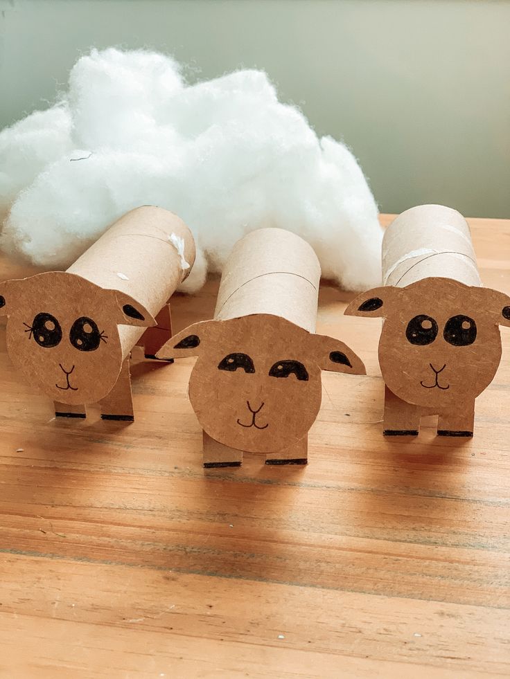 four sheep made out of toilet paper sitting on a wooden table next to cotton puffs