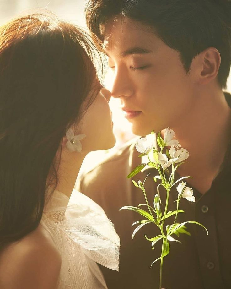 a young man and woman kissing each other while holding a flower in front of them