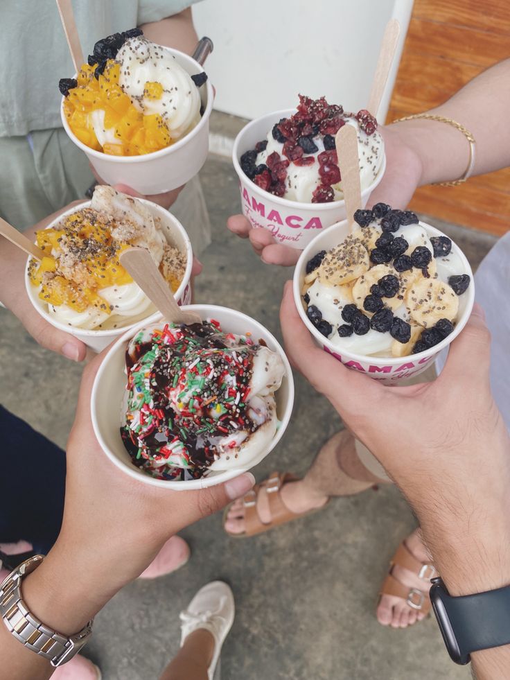 four people holding ice creams in their hands with toppings on each cup and spoon