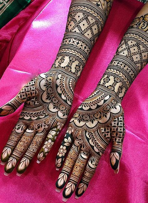 two hands with henna tattoos on them sitting on a pink cloth covered tablecloth