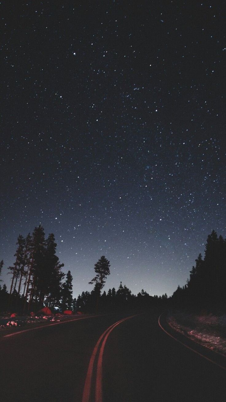 the night sky is filled with stars and cars driving on a road in front of some trees