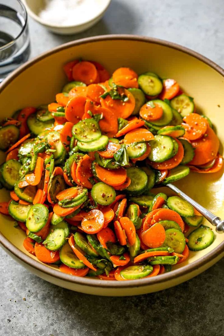 a bowl filled with sliced up veggies on top of a table next to two glasses