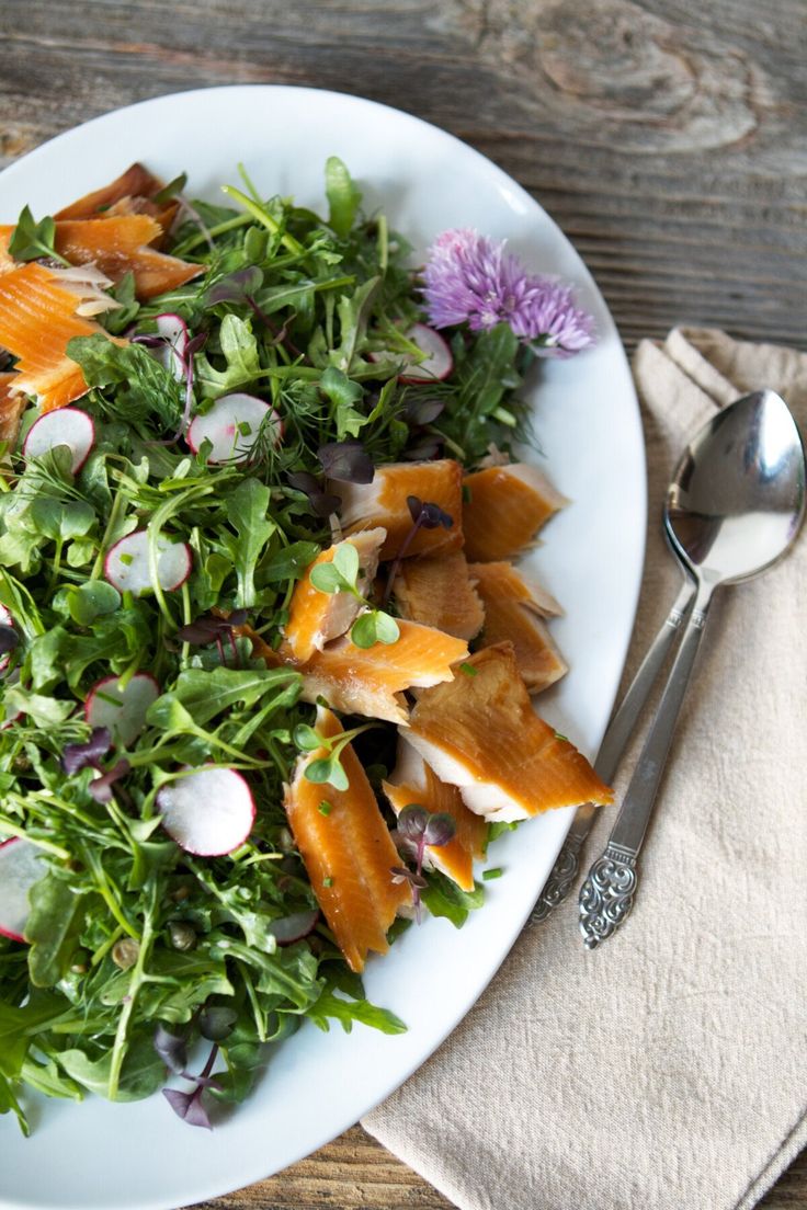 a white plate topped with salad next to a fork and napkin on top of a wooden table