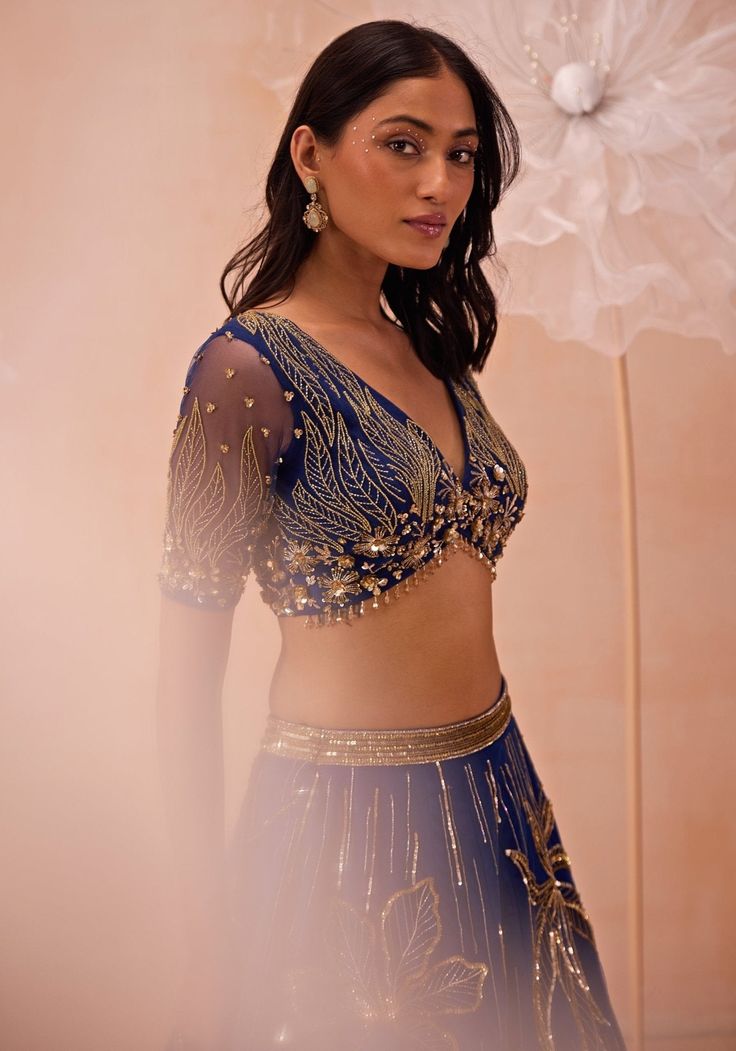 This exquisite Blue Embellished Lehenga set, crafted from delicate net fabric, perfectly blends traditional charm and contemporary elegance. The blue lehenga is heavily embellished with large, intricate floral motifs and linear designs, created using a stunning combination of zari, sequins, beads, and cutdana work. The richly adorned skirt is paired with a matching blouse that features complementary embroidery, adding to the overall opulence of the ensemble. The sheer dupatta drapes gracefully, enhancing the outfit's allure. A perfect lehenga for a cocktail party or a Sangeet party. Composition : Blouse, Lehenga & Dupatta : Net Care: Dry Clean Only and Vacuum Storage This product can be customized for sleeves, length and colour Delivery : 4-6 weeks as the product is hand crafted. Check Siz Zari Lehenga, Embellished Lehenga, Sheer Dupatta, Cutdana Work, Pre Bridal, Ethnic Wears, Blouse Lehenga, Lehenga Pattern, Choli Dress