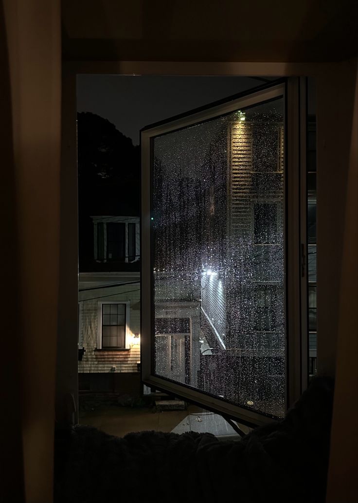 an open window at night with rain falling on the glass and light shining through it