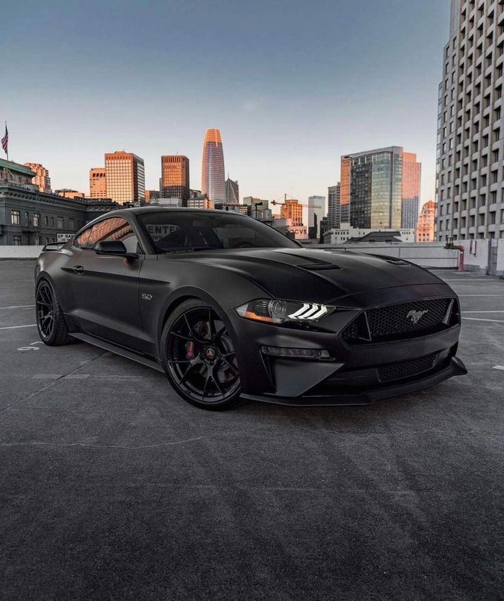 a black mustang parked in a parking lot with the city skyline in the back ground