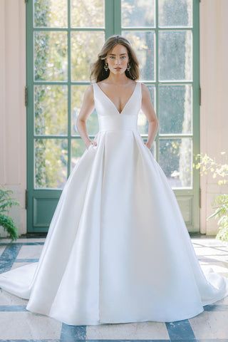 a woman standing in front of a window wearing a white wedding dress with a deep v - neckline