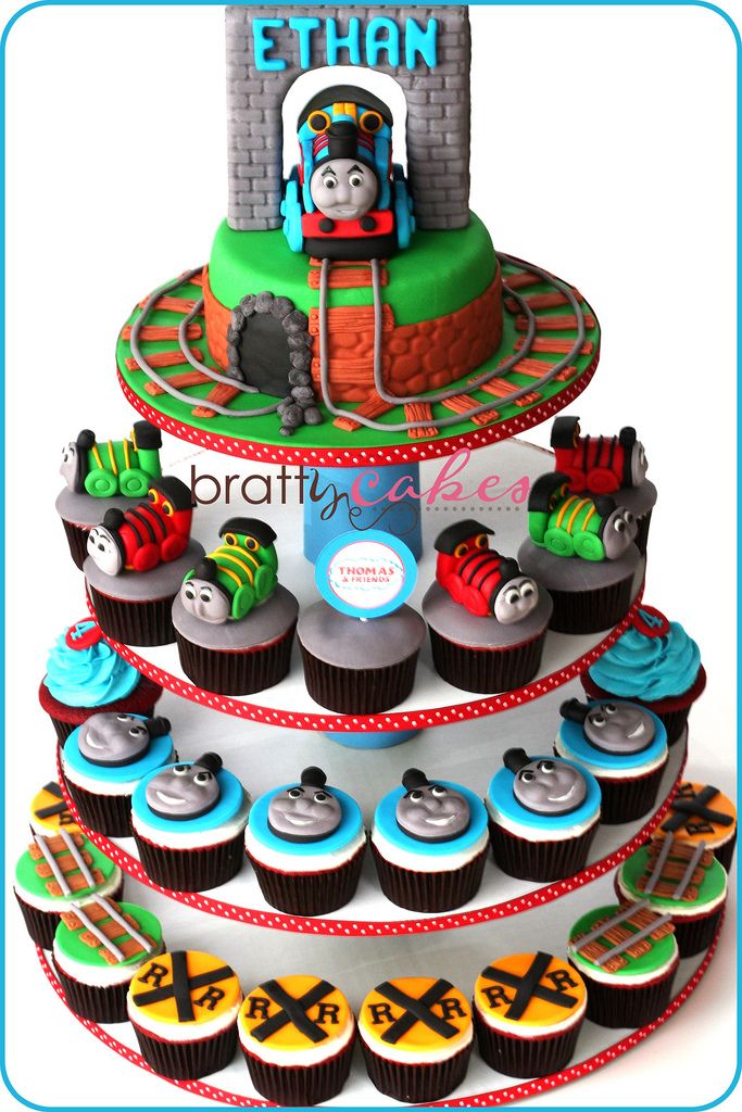 a thomas the train birthday cake with cupcakes and decorations on it's tier