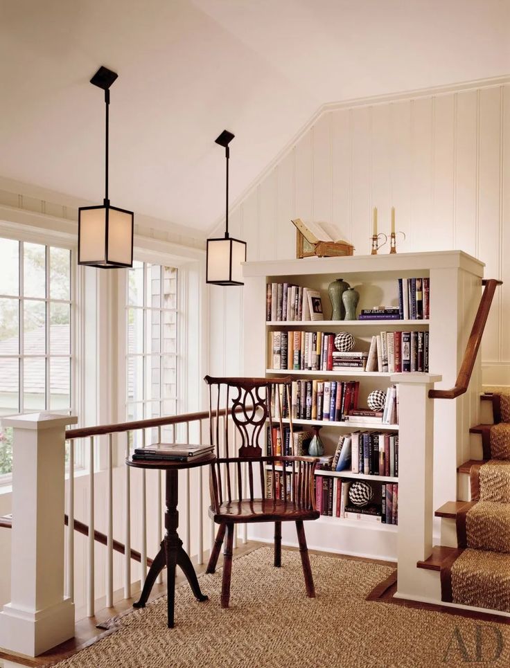 a room with stairs, bookshelf and table in front of windows on the second floor