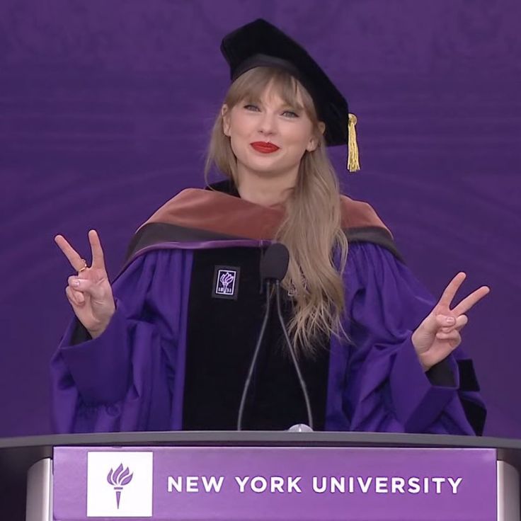 a woman in a graduation gown giving a speech at a podium with her hands up