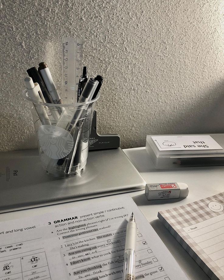 an office desk with pens and paper on it, next to a pen holder that has several different types of pens in it