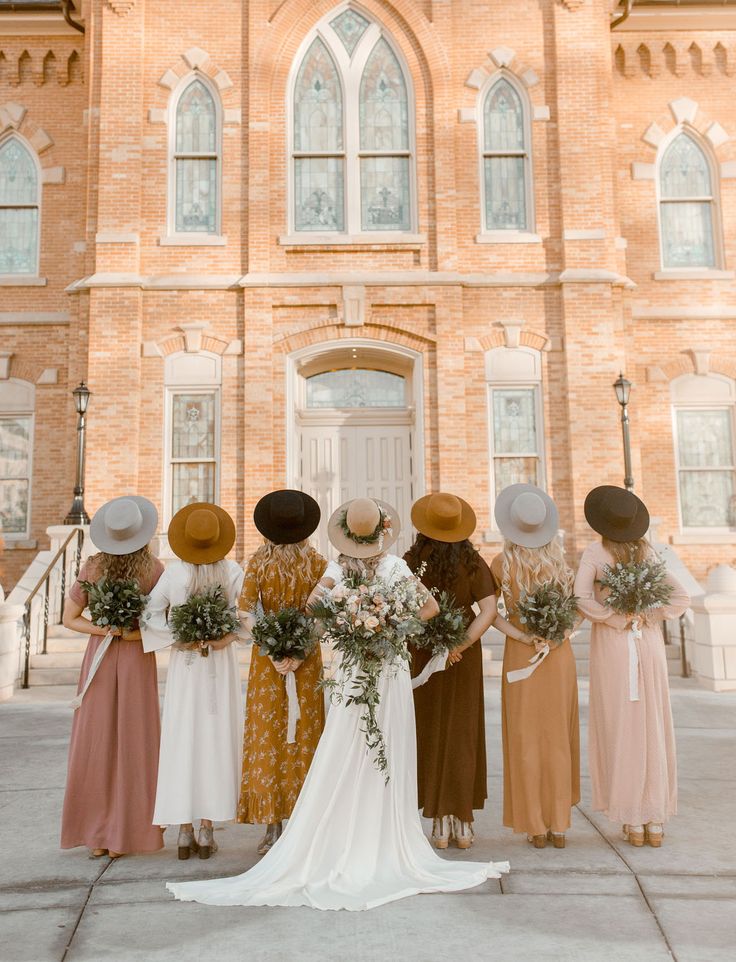 a group of bridesmaids standing in front of a church with their bouquets