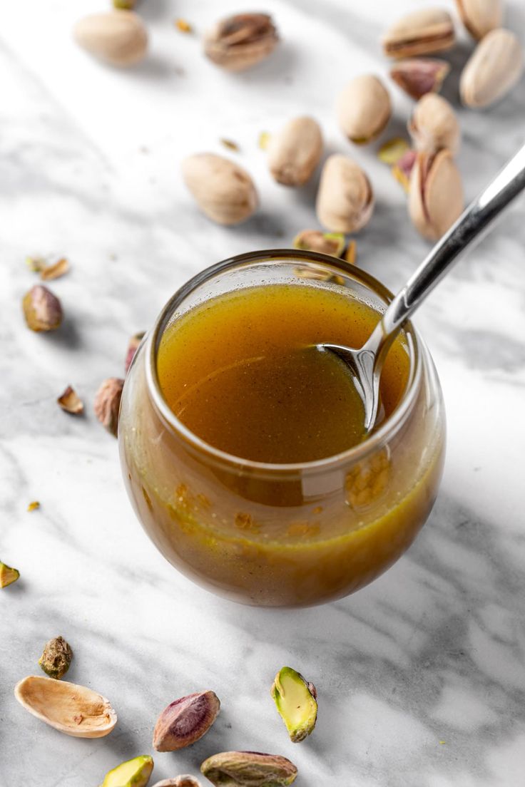 a glass jar filled with liquid sitting on top of a marble table next to nuts