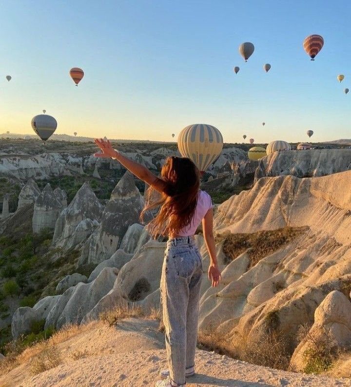 a woman standing on top of a hill with hot air balloons flying in the sky