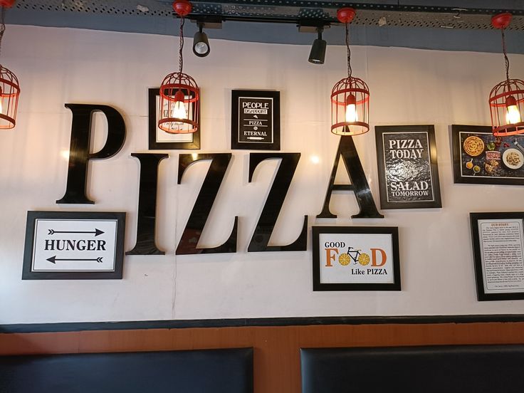 several framed pizzas are hanging on the wall in a pizzeria with red lanterns