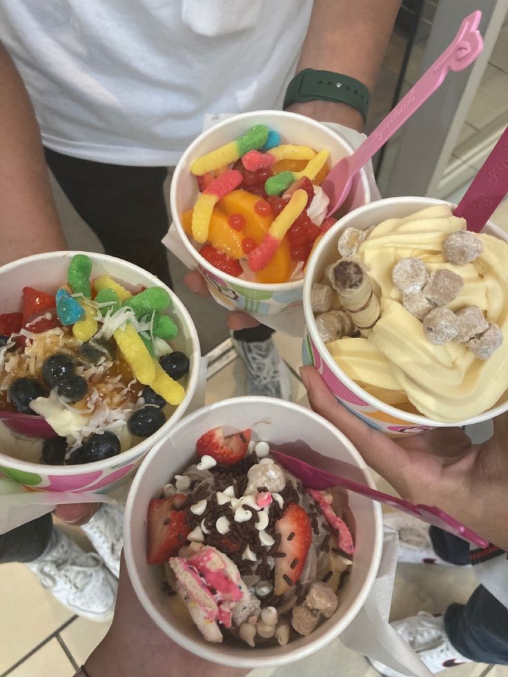 three people holding up bowls of fruit and ice cream