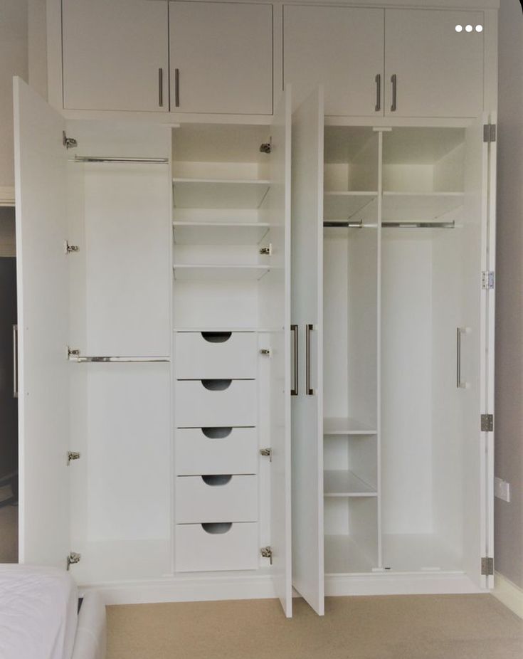 an empty bedroom with white closets and drawers on the wall, in front of a bed