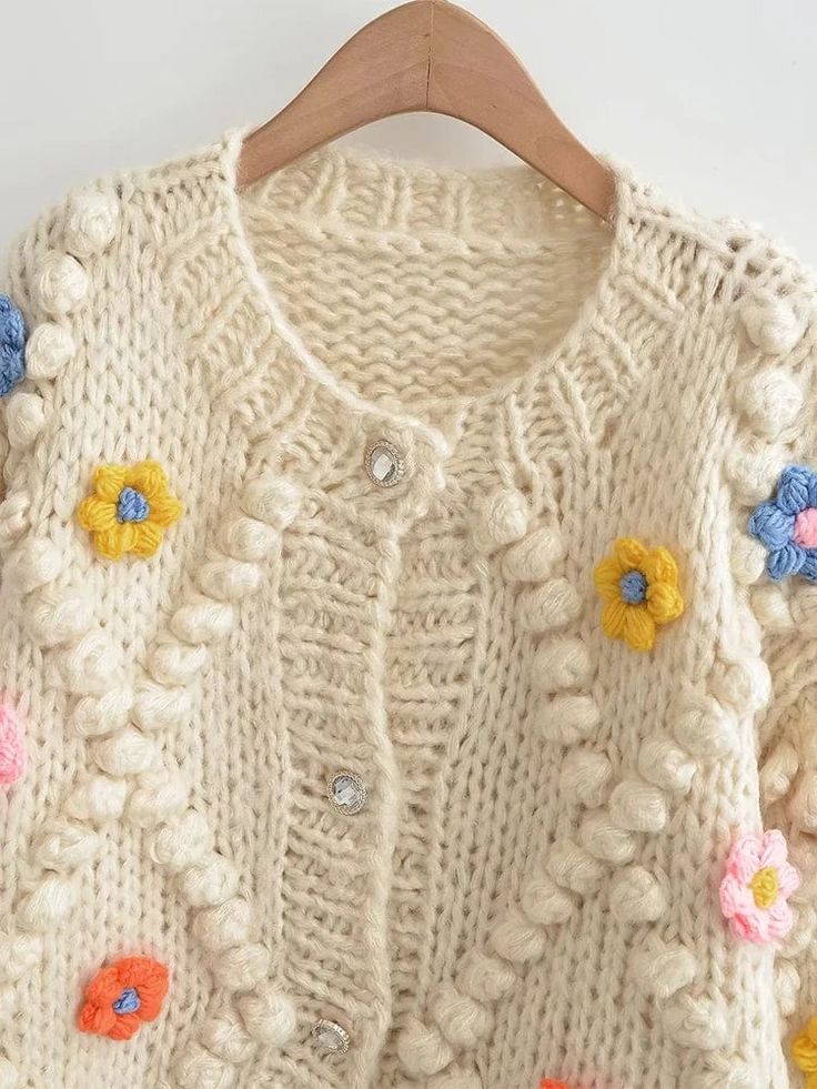 a white sweater with colorful flowers on the front and back, hanging from a wooden hanger