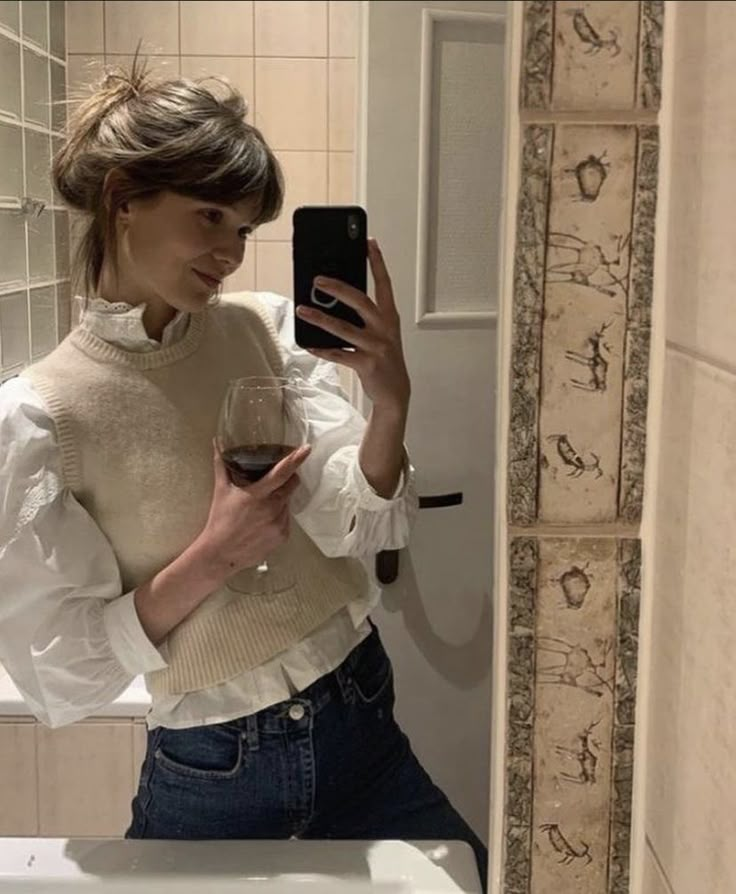 a woman is taking a selfie in the bathroom with her cell phone and holding a glass of wine