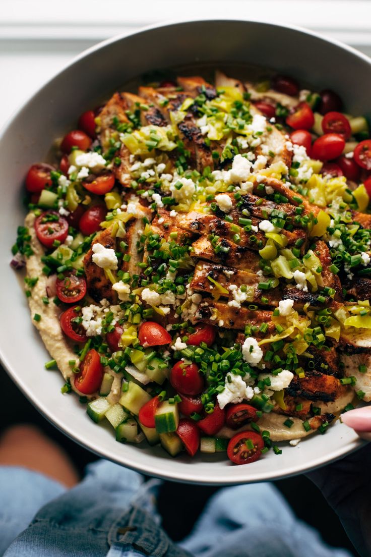 a person holding a white bowl filled with lots of food on top of a table