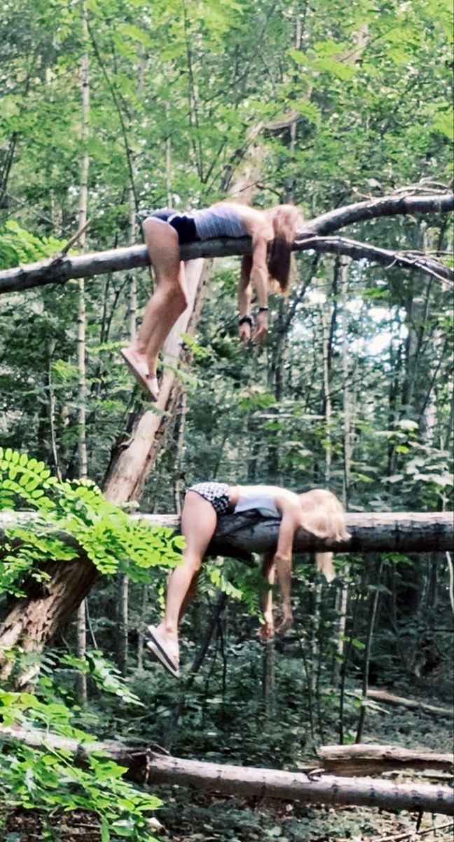 two people are hanging upside down in the woods, one is on a fallen tree