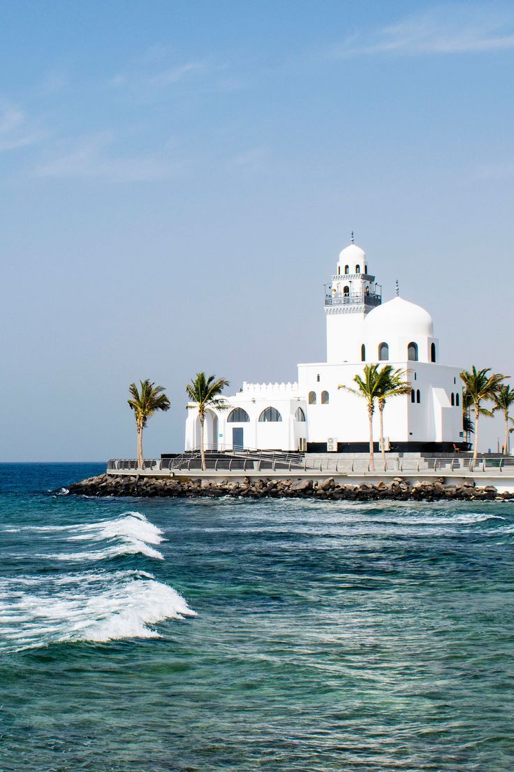 a white building sitting on top of a pier next to the ocean with palm trees