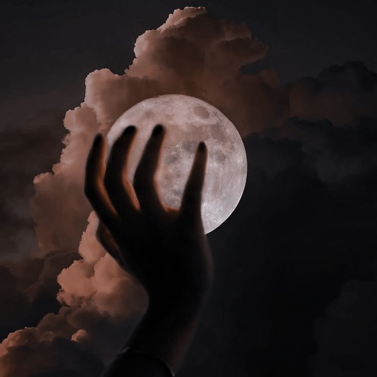 a person's hand reaching up into the sky with a full moon in the background