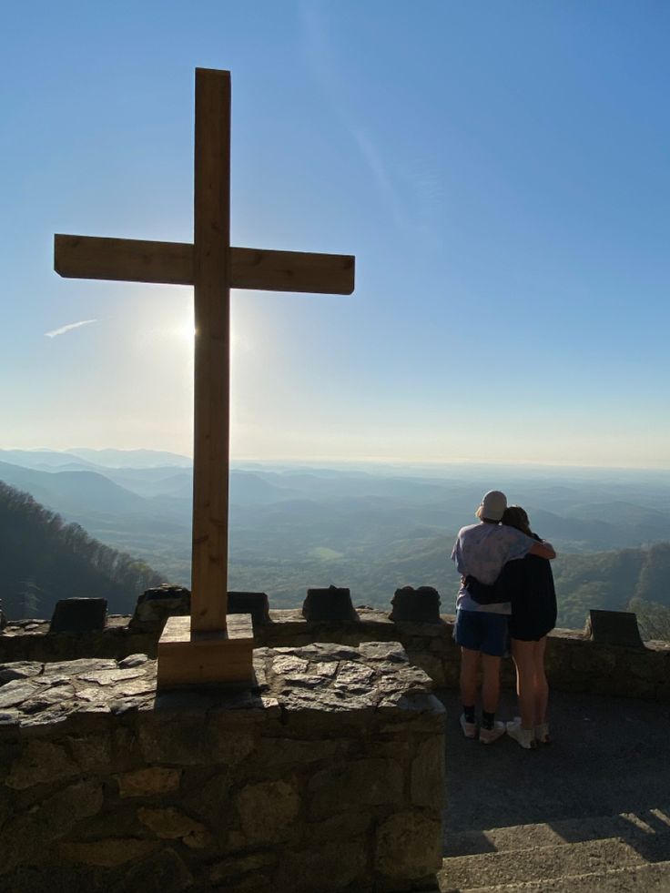 two people standing at the top of a hill with a cross in front of them