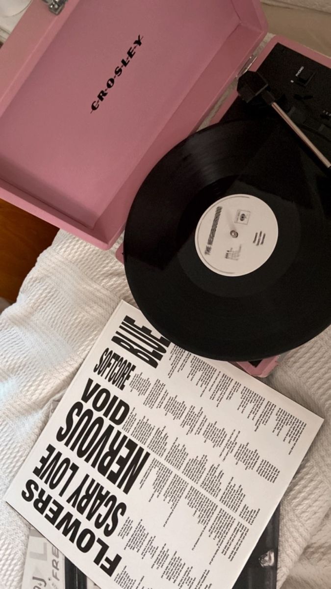 a record player sitting on top of a bed next to a pink box and magazine