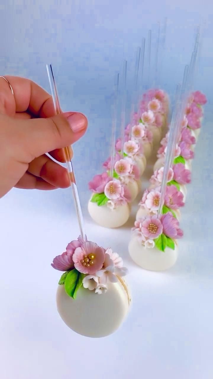 a hand is holding a pen over some cake pops with flowers on them and white icing