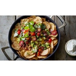 a skillet filled with nachos and toppings next to a bowl of sour cream