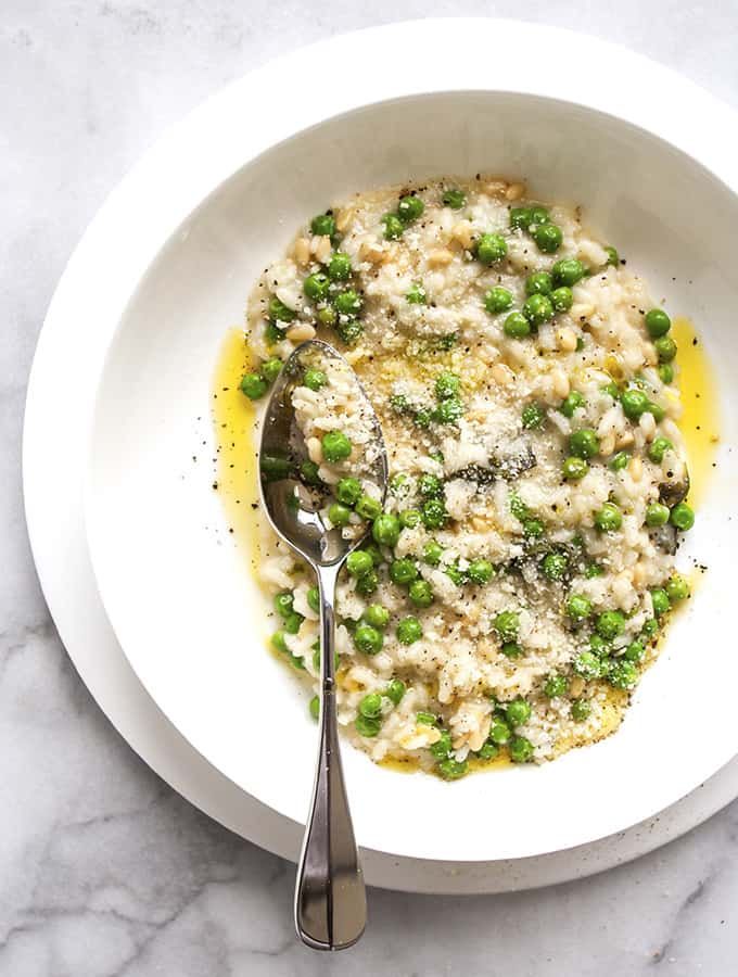 a white bowl filled with rice and peas on top of a marble table next to a spoon