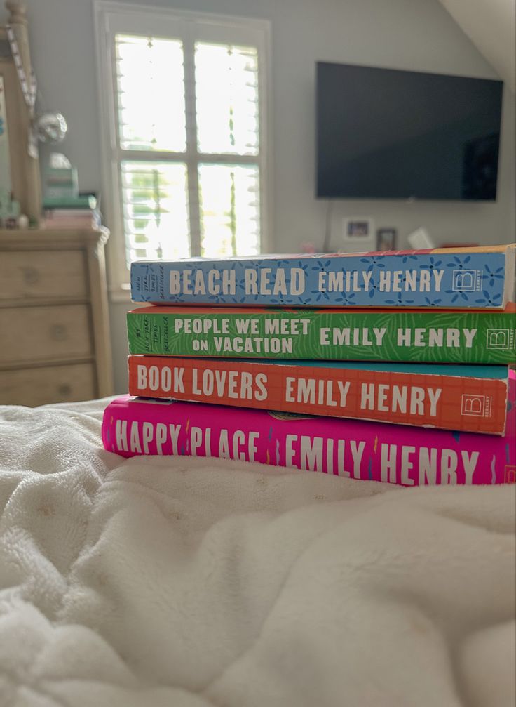 four books stacked on top of each other in front of a bed with white sheets