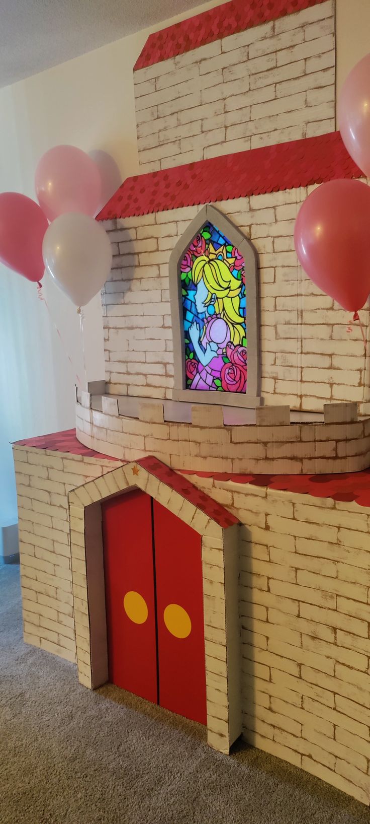 a castle made out of cardboard with balloons in front of it and a stained glass window