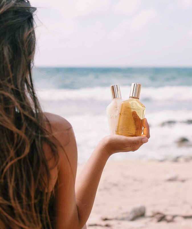 a woman holding two bottles of perfume in front of her face and body on the beach