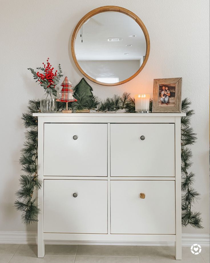 a white dresser with christmas decorations on top and a round mirror above it, along with candles