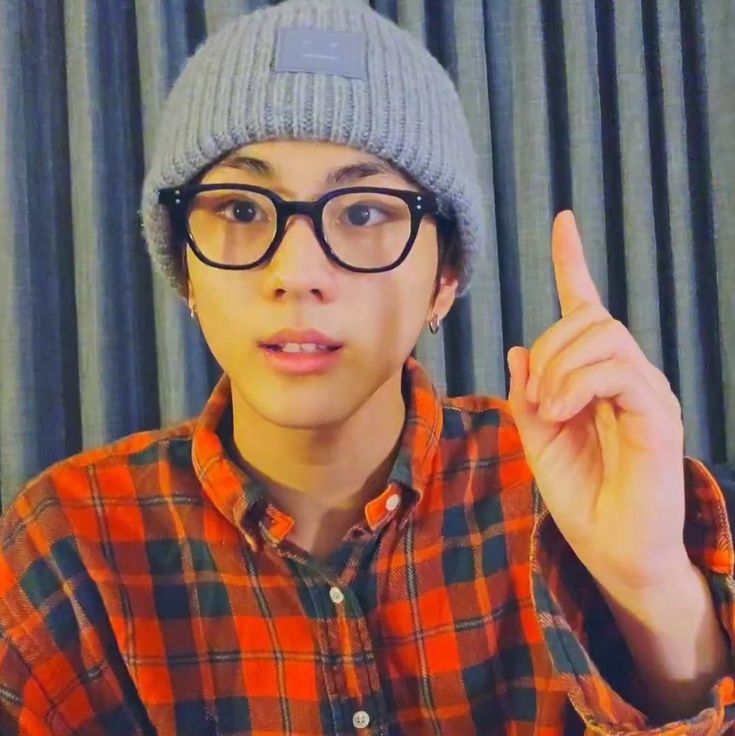 a young man wearing glasses and a beanie gives the peace sign with his hand