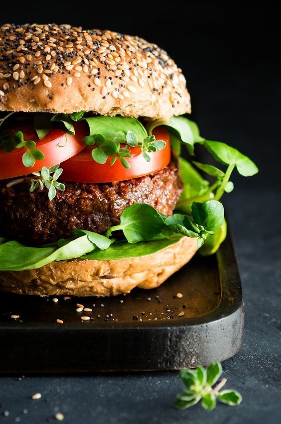 a hamburger with lettuce, tomato and cheese on it sitting on a black tray